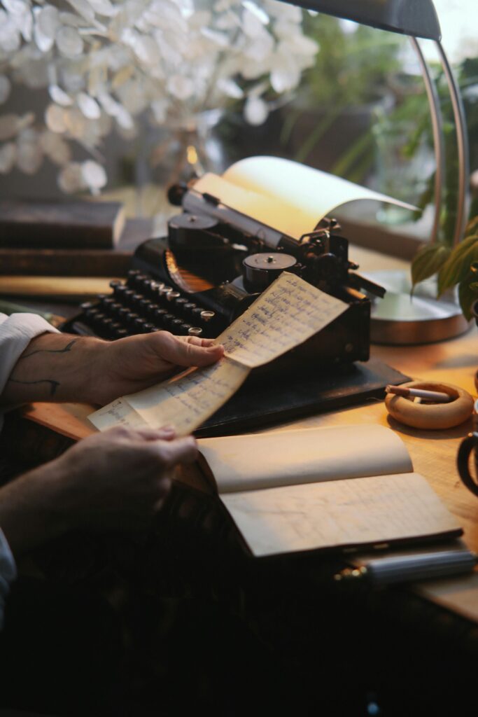 Hands working with paper and a typewriter on a wooden desk in a cozy, plant-filled study setting.