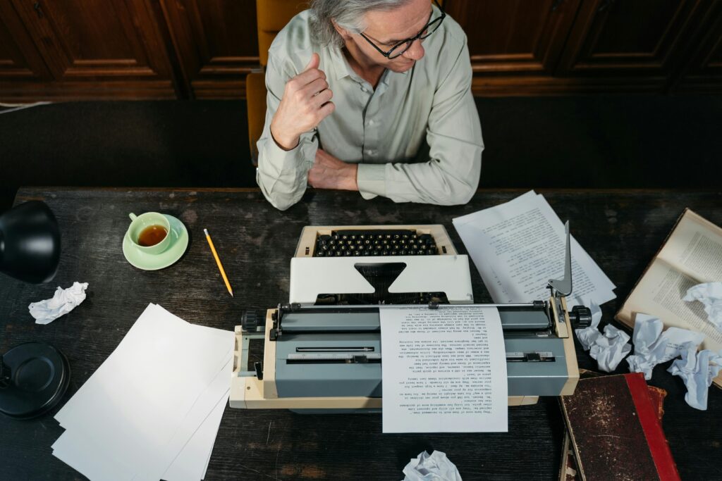 An overhead shot of an adult man writing with a typewriter in a vintage-themed study.